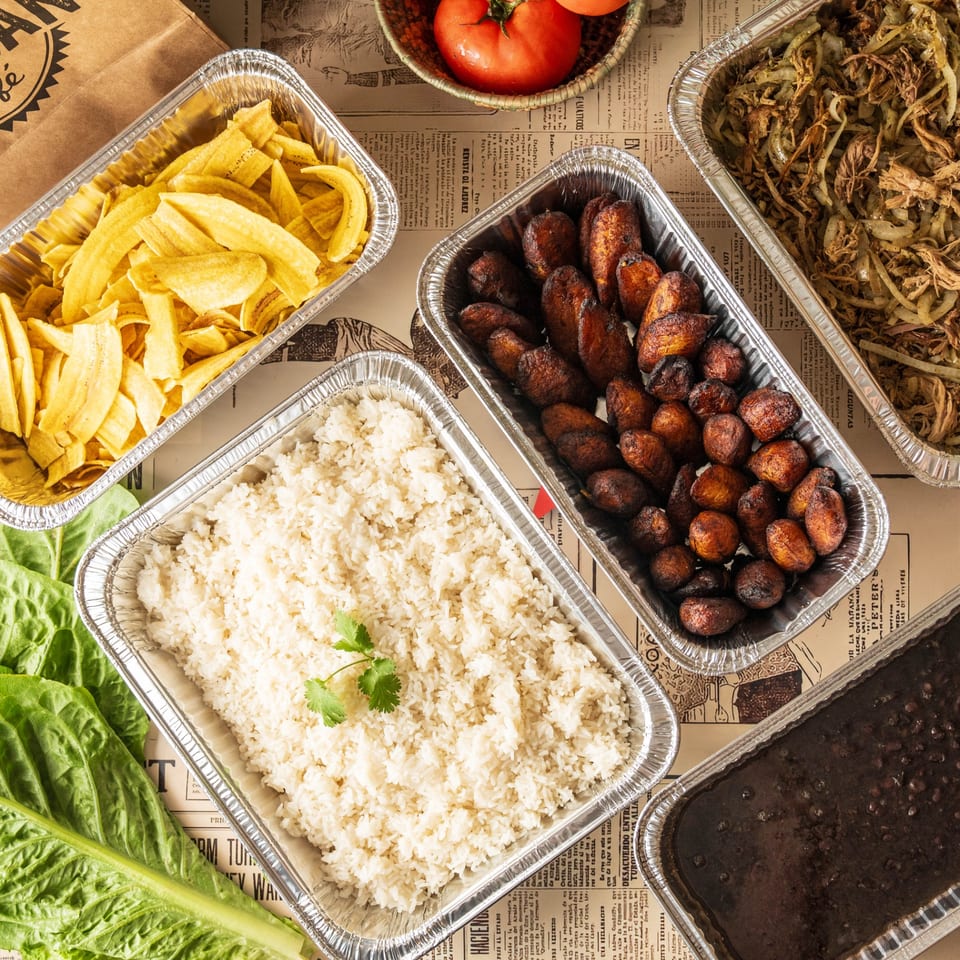 Cuban dishes in foil containers: plantain chips, white rice, black beans, fried plantains, and shredded beef.