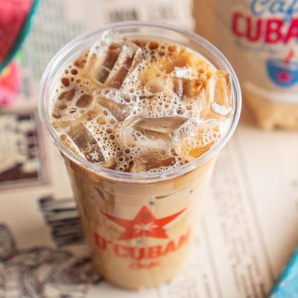 Iced D'Cuban Cafe coffee with ice and foam in a clear plastic cup.