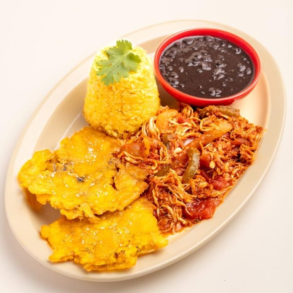 A Cuban meal with yellow rice, black beans, shredded chicken, and fried plantains on an oval plate.