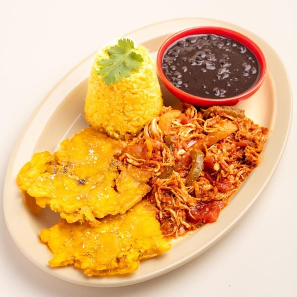 A Cuban meal with yellow rice, black beans, shredded chicken, and fried plantains on an oval plate.