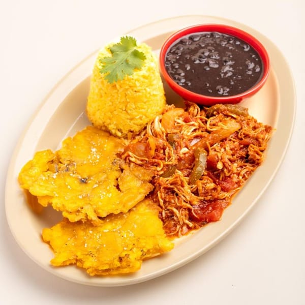 A Cuban dish with yellow rice, black beans, shredded chicken, and two fried plantains.