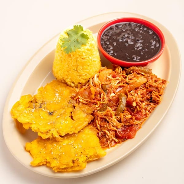 Cuban shredded chicken with yellow rice, black beans, and two fried plantains on a white plate.