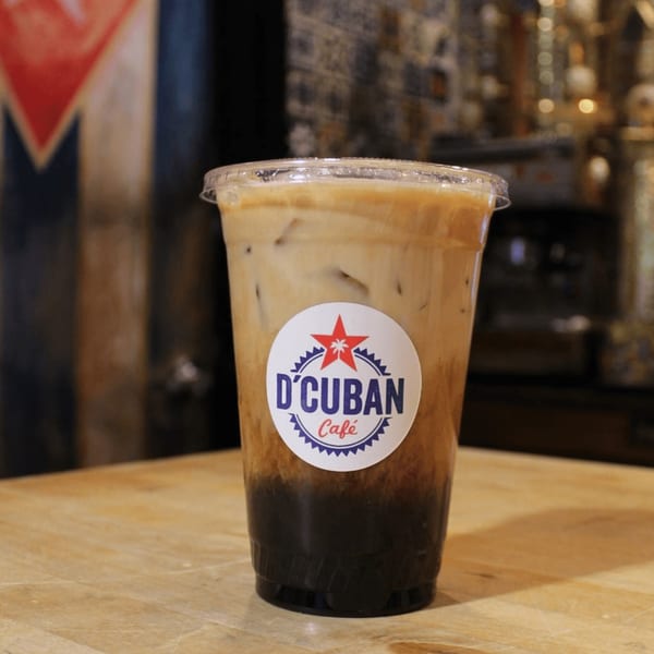 Iced coffee with milk and ice in a D'Cuban Cafe branded cup on a wooden table.