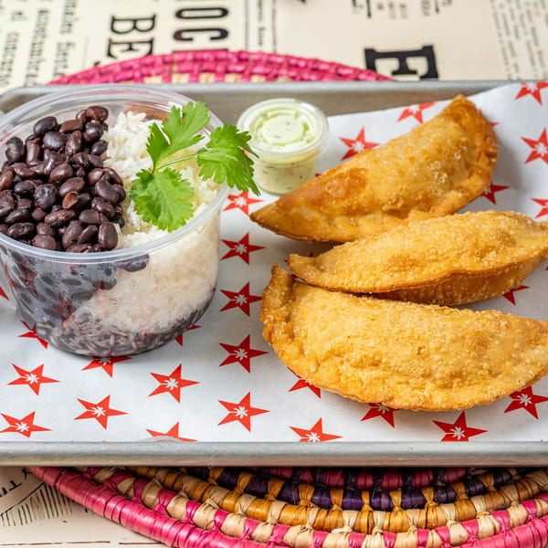 Cuban meal with black beans, white rice, cilantro, three empanadas, and a side of green sauce.